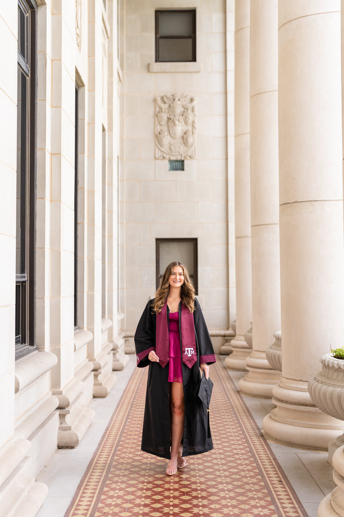 Texas A&M senior girl walking while wearing gown and Aggie stole and smiling in columns of the Administration Building