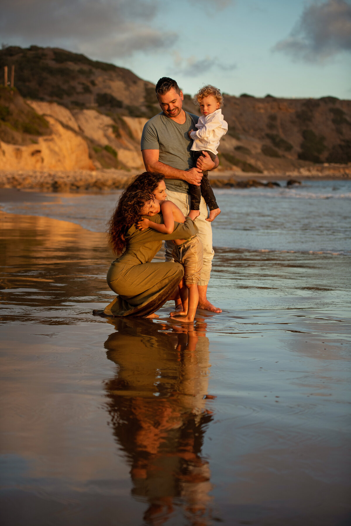 Loving family of four during lifestyle photoshoot at Palos Verdes beach in California hugging each other and showing love.