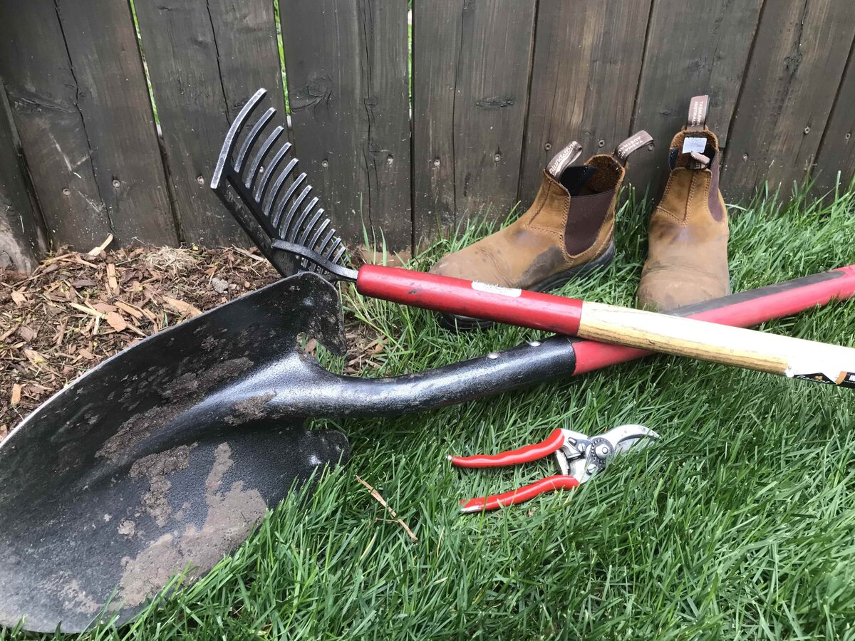 Gardening tools, a rake, shovel, clippers and workboots sit on the grass