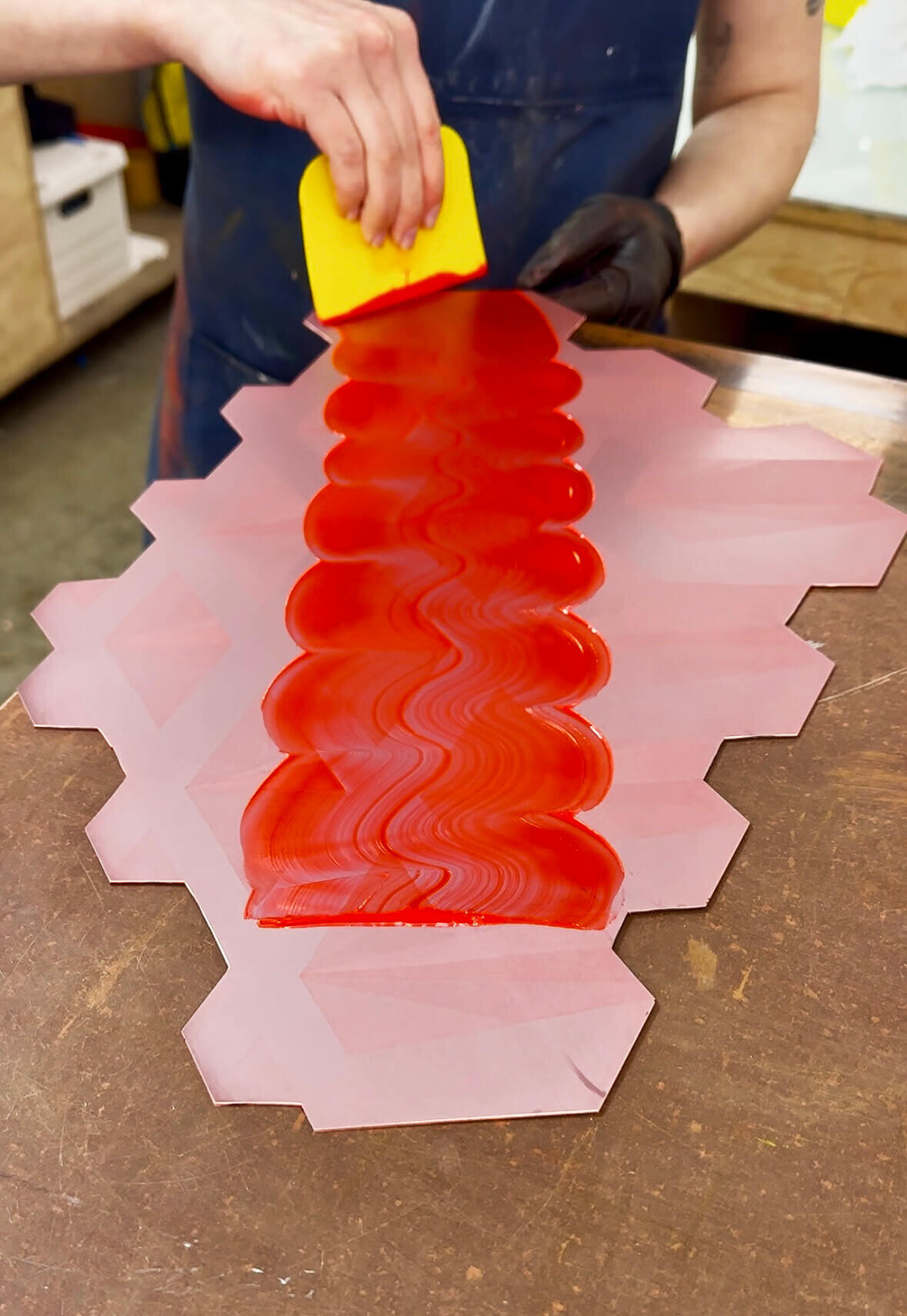 A wide swath of glossy red ink being applied to a custom-cut hexagonal printing plate.