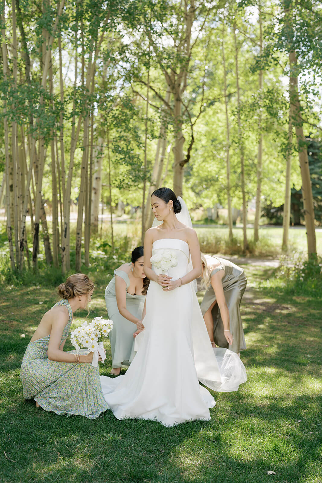 Bridesmaids fluff the wedding dress of the bride before she walks down the aisle at her Aspen Meadows Resort outdoor weddding.