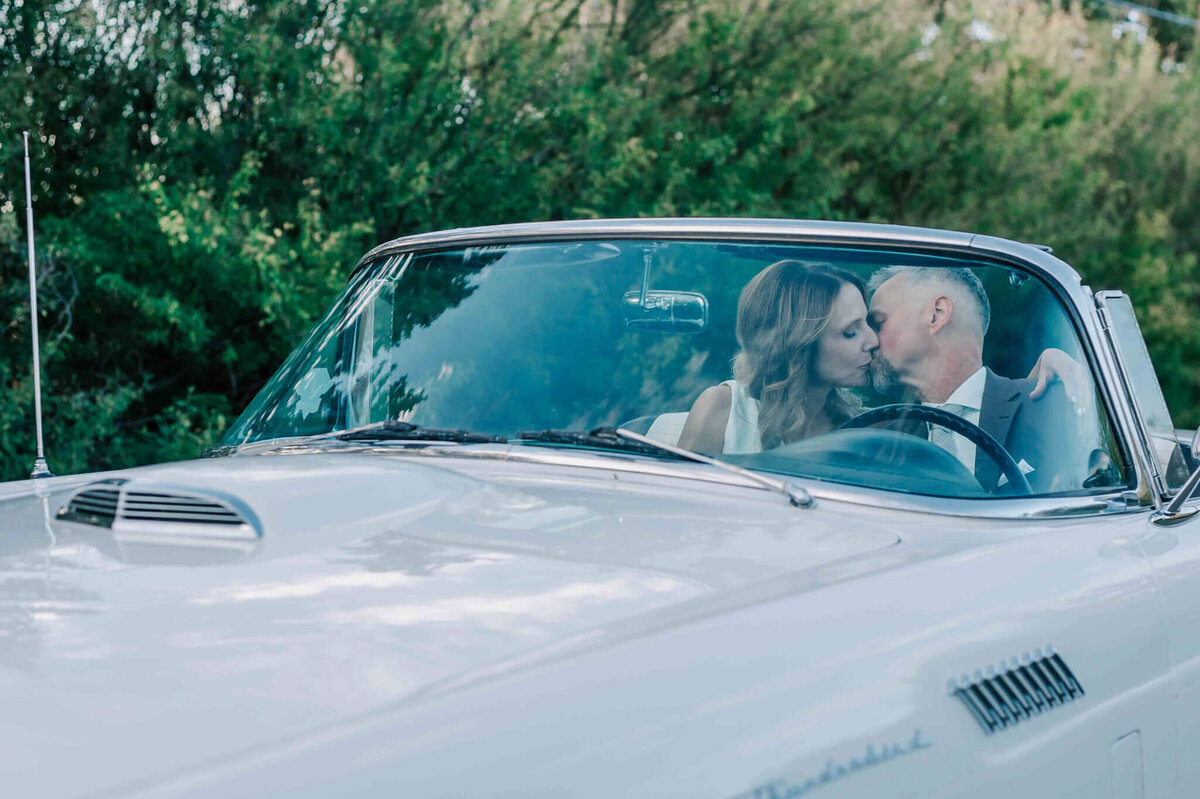 bride and groom kiss in the front seat.