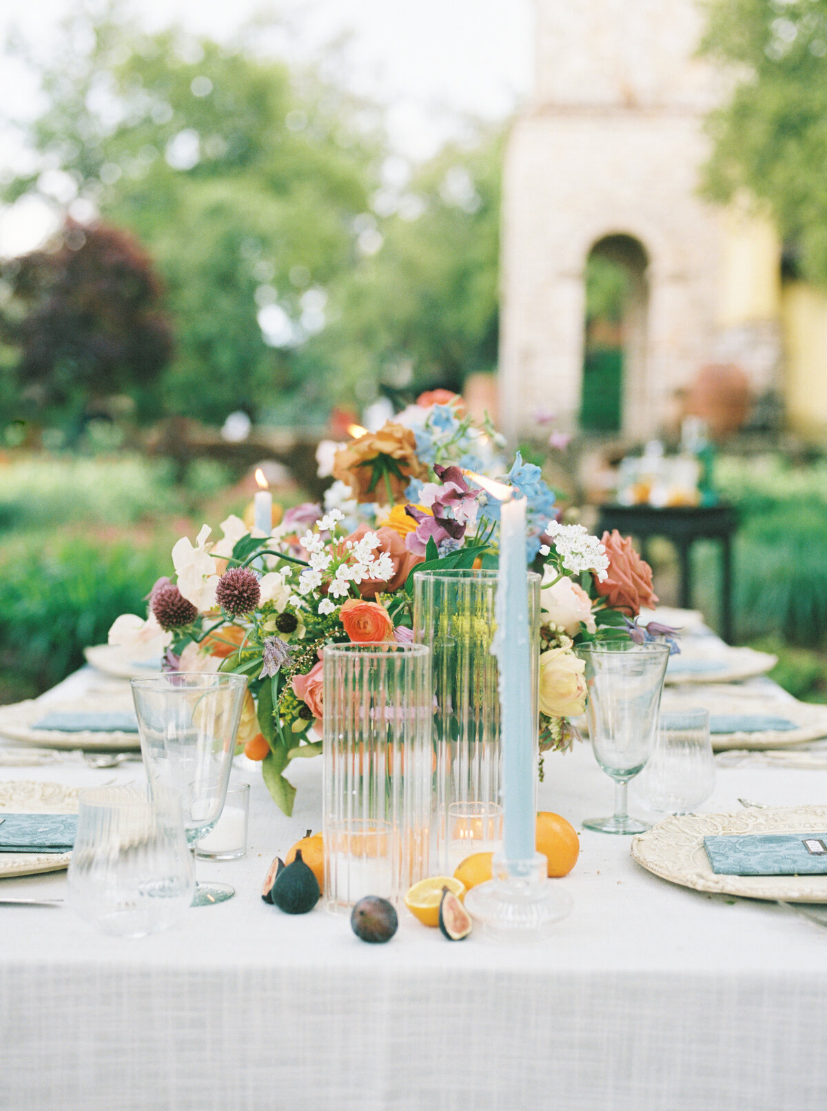 closeup of centerpieces on table taken on medium format film with blue candlesticks, figs, oranges, white patterned tablecloth, and colorful florals in Texas