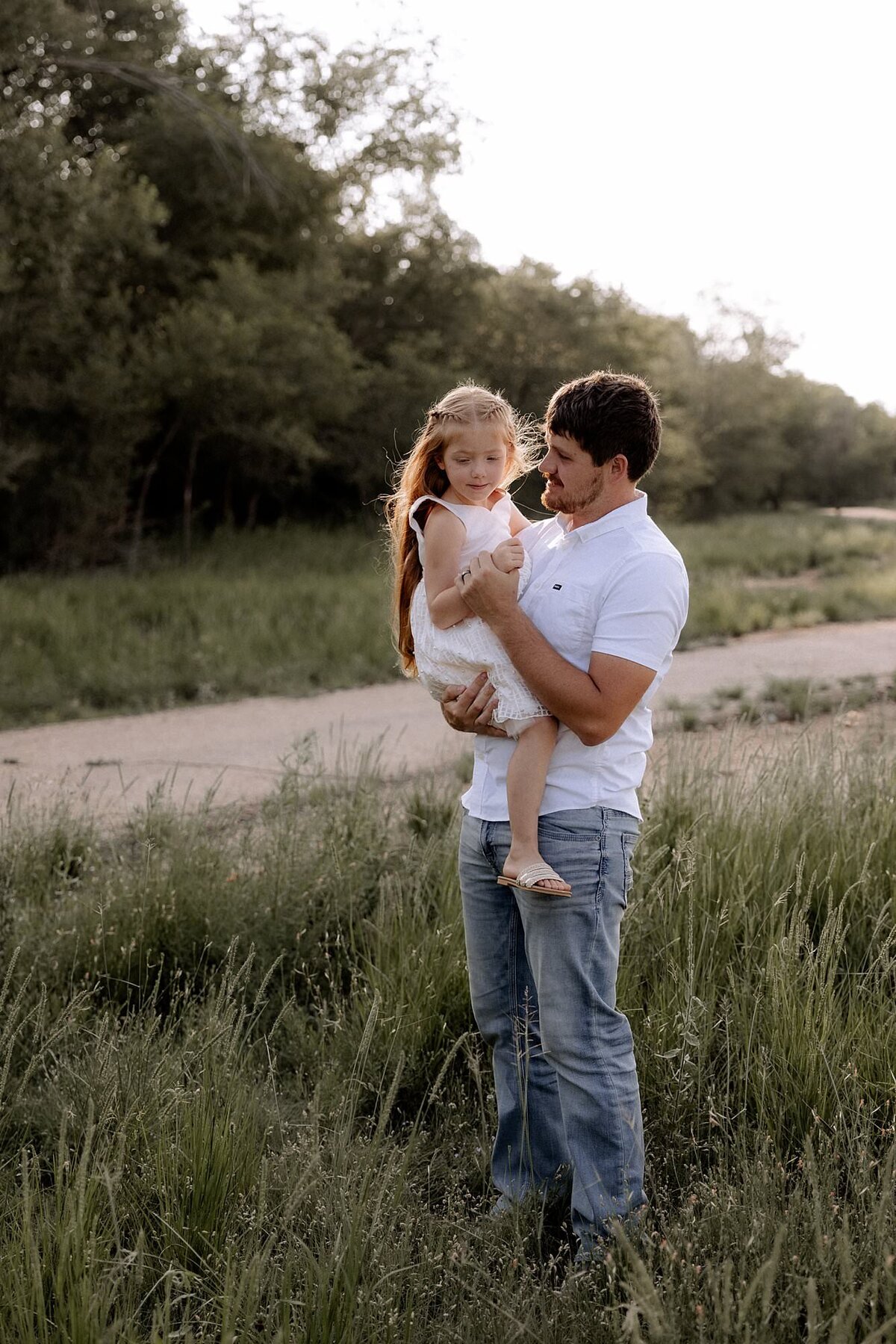 Dad holding his daughter in a grass field dancing with her.