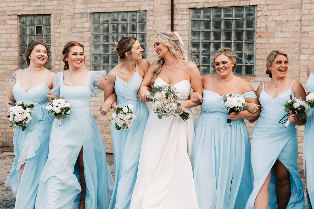 A bride walks with her bridesmaids in light blue dresses in an alley
