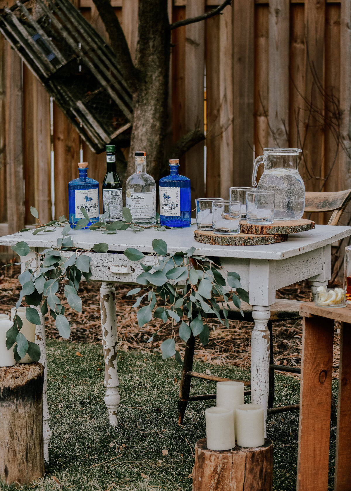 A rustic table set up outside at a wedding or event with gin, greenery and candles.