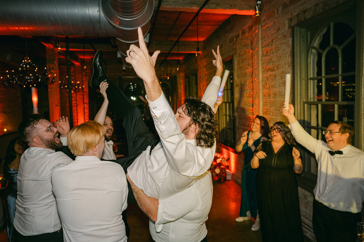  Groom lifted by guests on the dance floor under red ambient lighting at high-end San Antonio wedding celebration