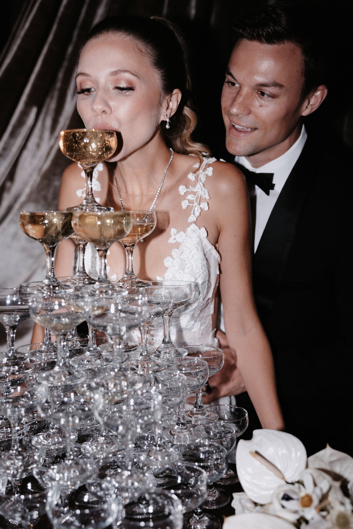 Elopement photography, bride sipping champagne from tower while groom holds her from behind smiling
