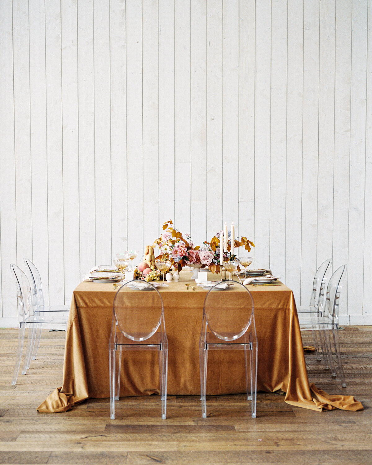 Table draped in golden velvet surrounded with ghost acrylic chairs and romantic florals on the ceterpice