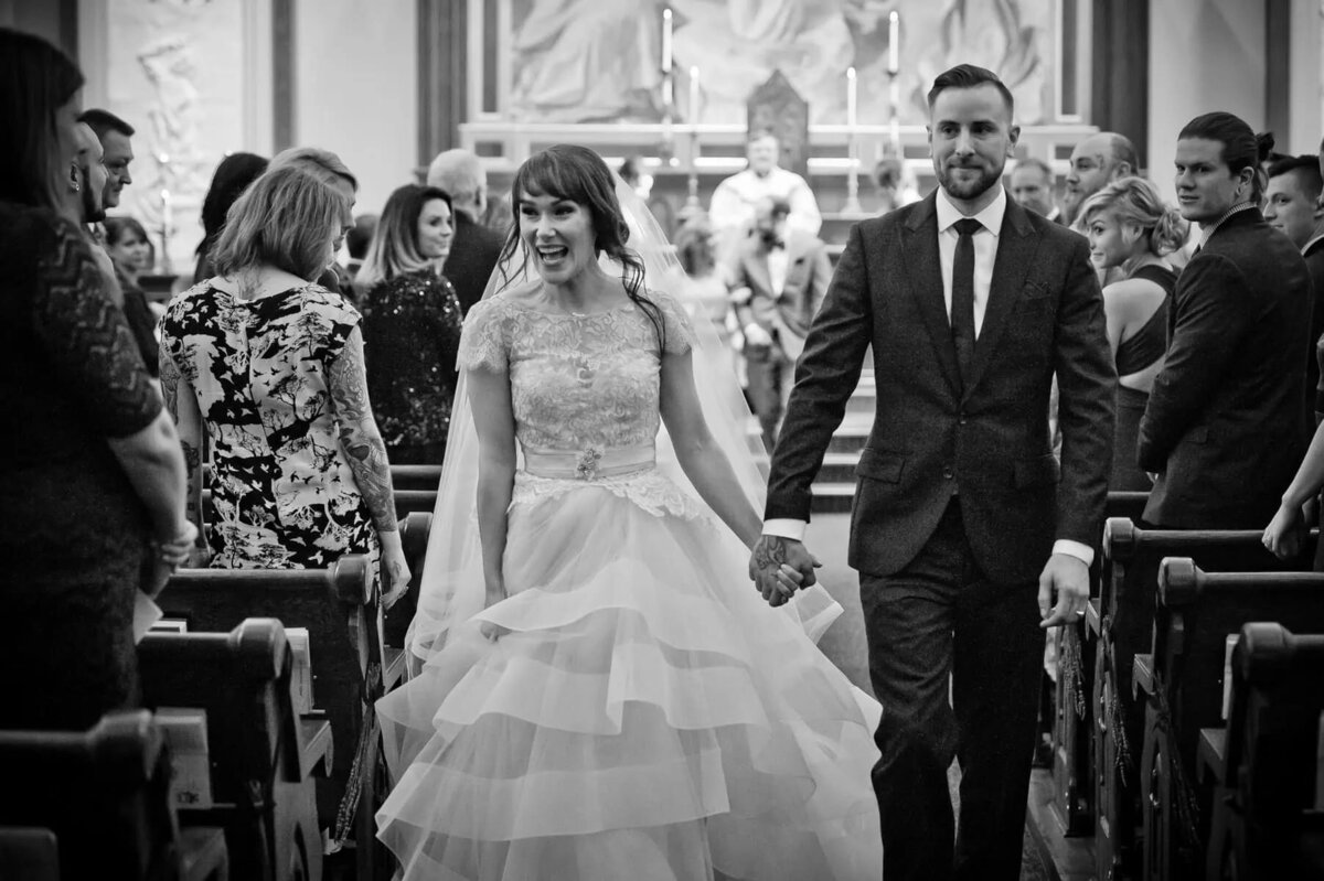 A bride and groom holding hands and walking back up the aisle.