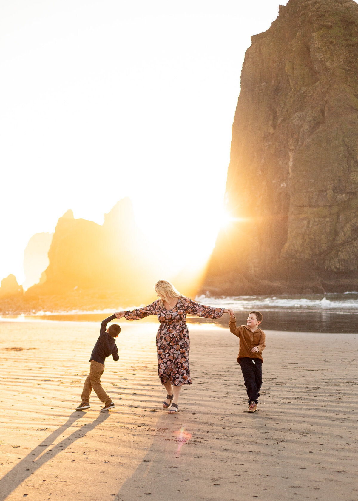 Mother and two sons dancing at sunset in front of Haystack Rock in Cannon Beach, Oregon. Photo by Portland family photographer.