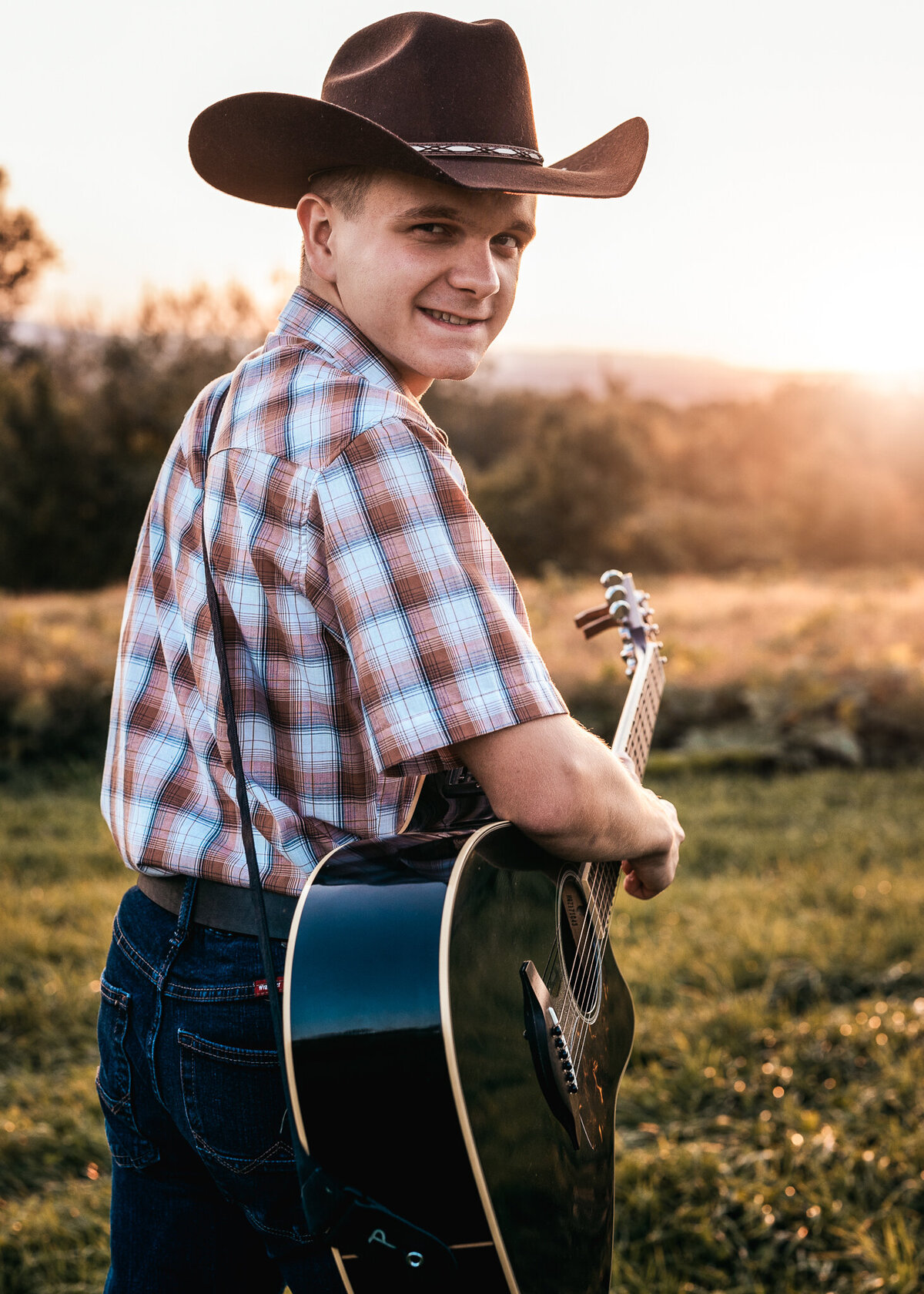 High School Senior play guitar at his photo session in open field at sunset by Lisa Smith Photography
