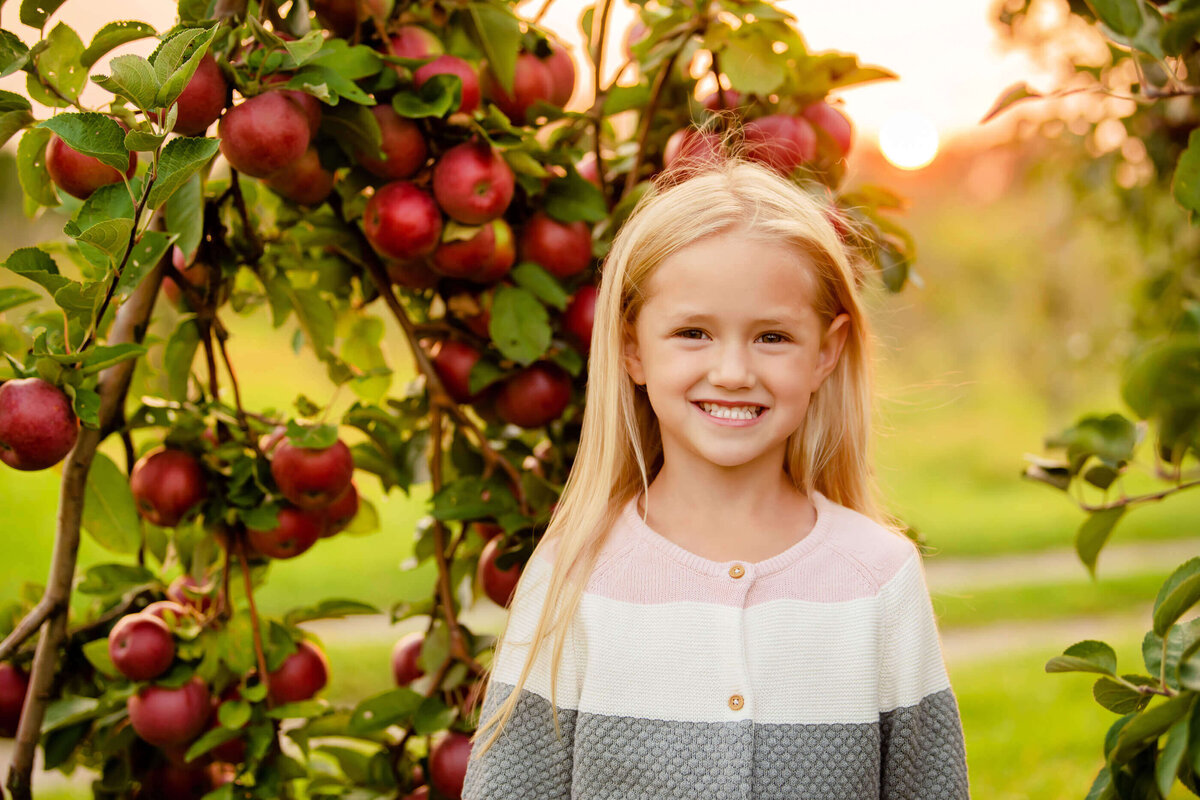 little girl standing under and apple tree with the golden light behind her for her fall family photos in Burlington, ON