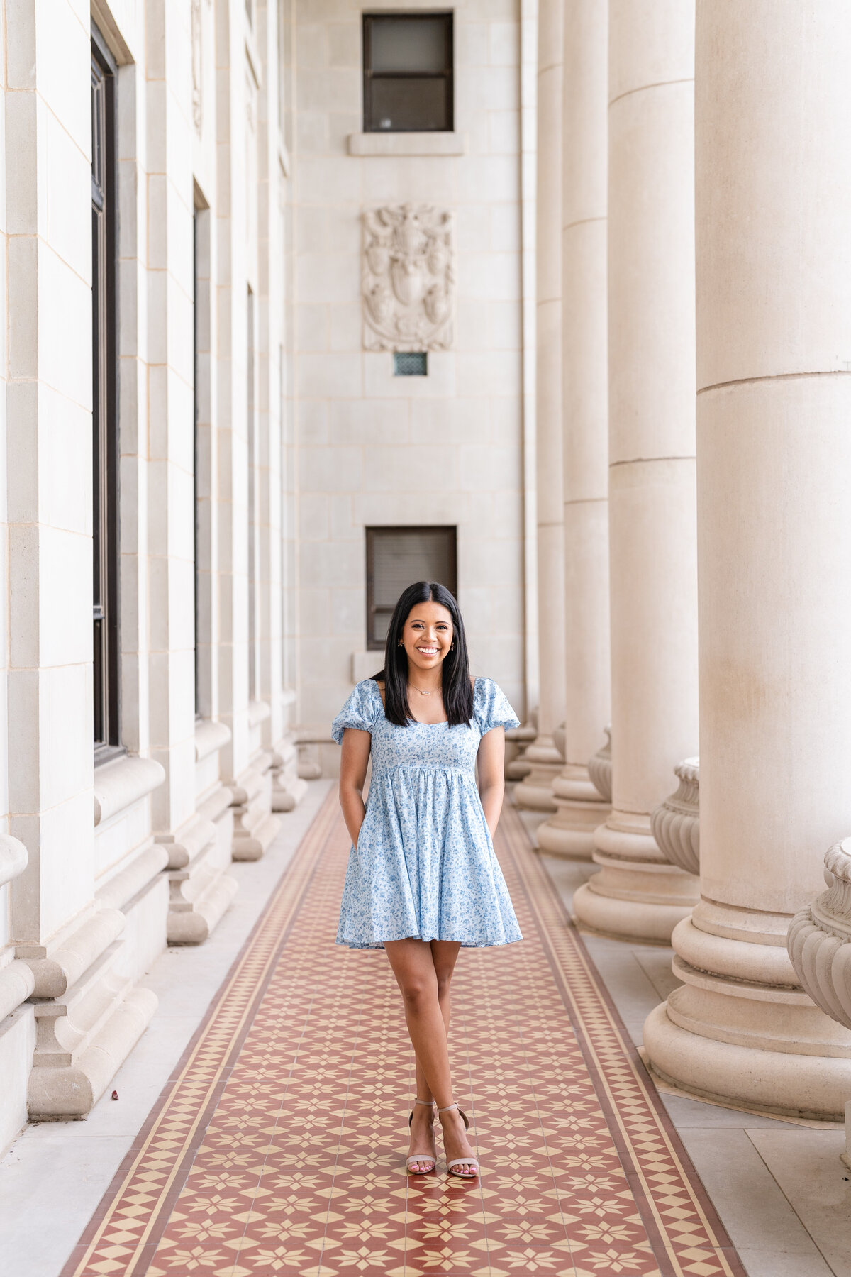 Texas A&M senior girl wearing blue dress with hands in pockets and smiling while standing in columns of Administration Building