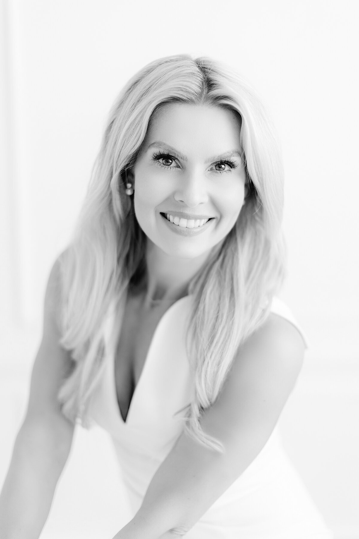 Close up black and white photo of a DFW business woman sitting on a chair in a DFW photography studio as she smiles at the camera for her professional headshots.