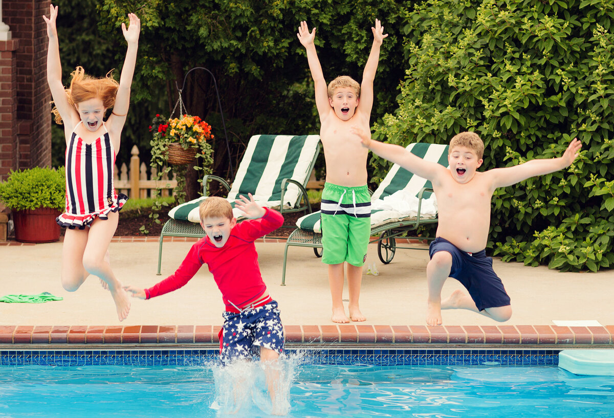 Cousins are jumping into the pool in bright colored suits. One boy pretended to start to jump and tricked the others!