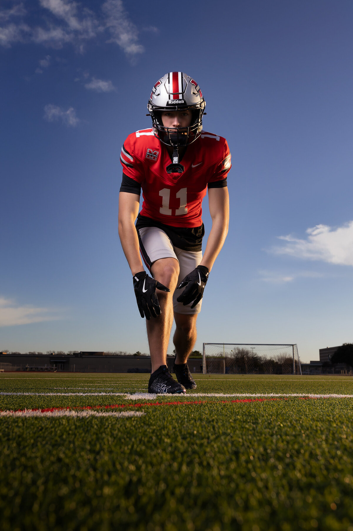 Senior football player in a red uniform with helmet, crouched on the field for an action-packed portrait in Dallas, highlighting athleticism and determination for a senior photoshoot.