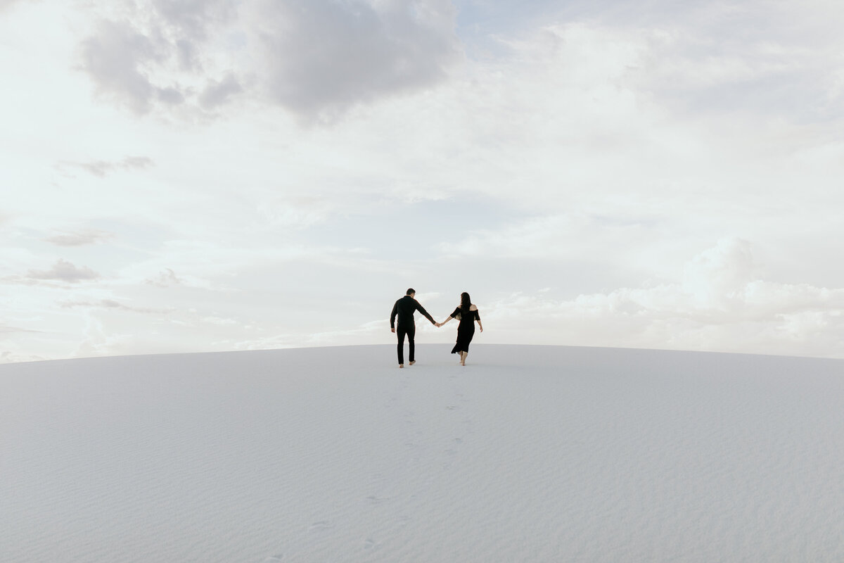 man and woman holding hands walking together at white sands NP