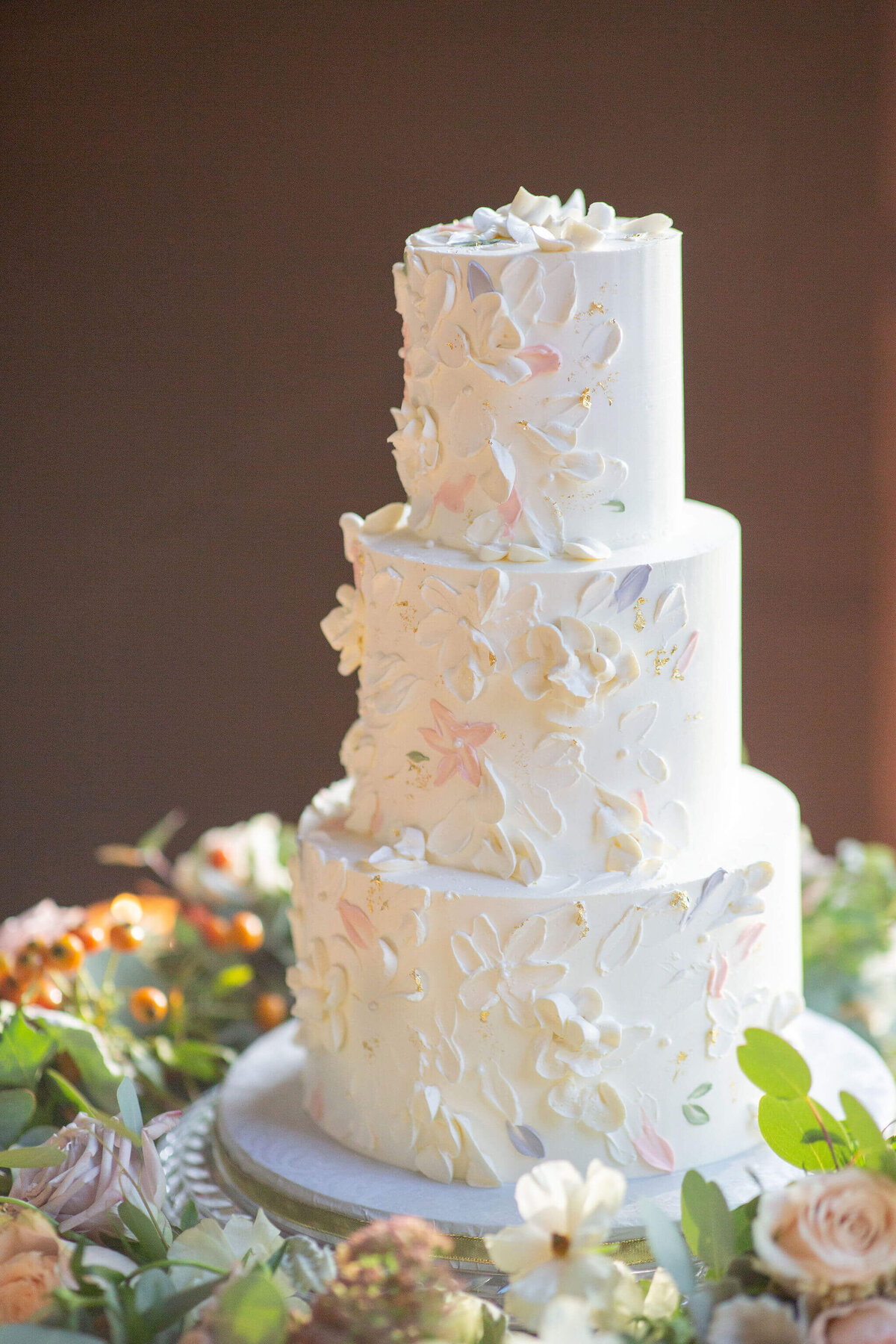 three -tiered wedding cake surrounded by flowers