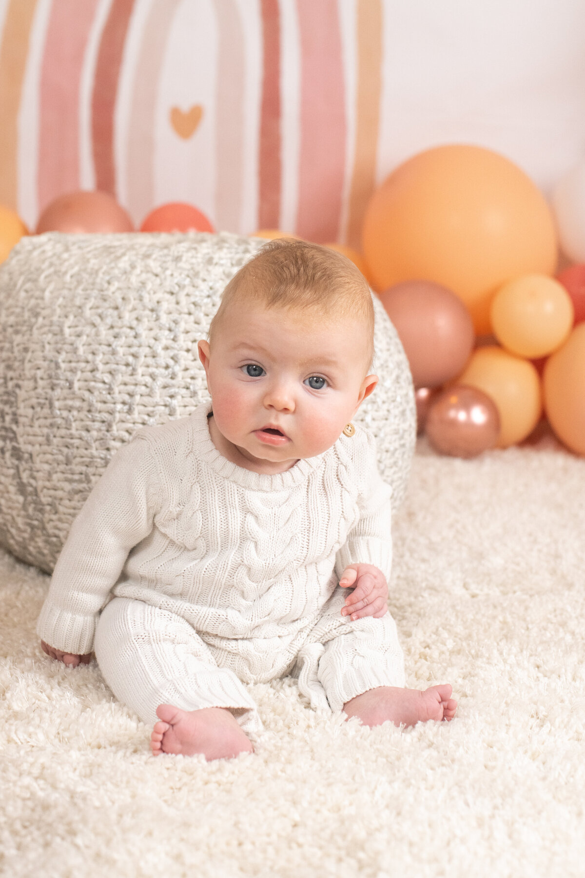 four month old baby sitting up on Valentine's set with pink rainbow and balloons