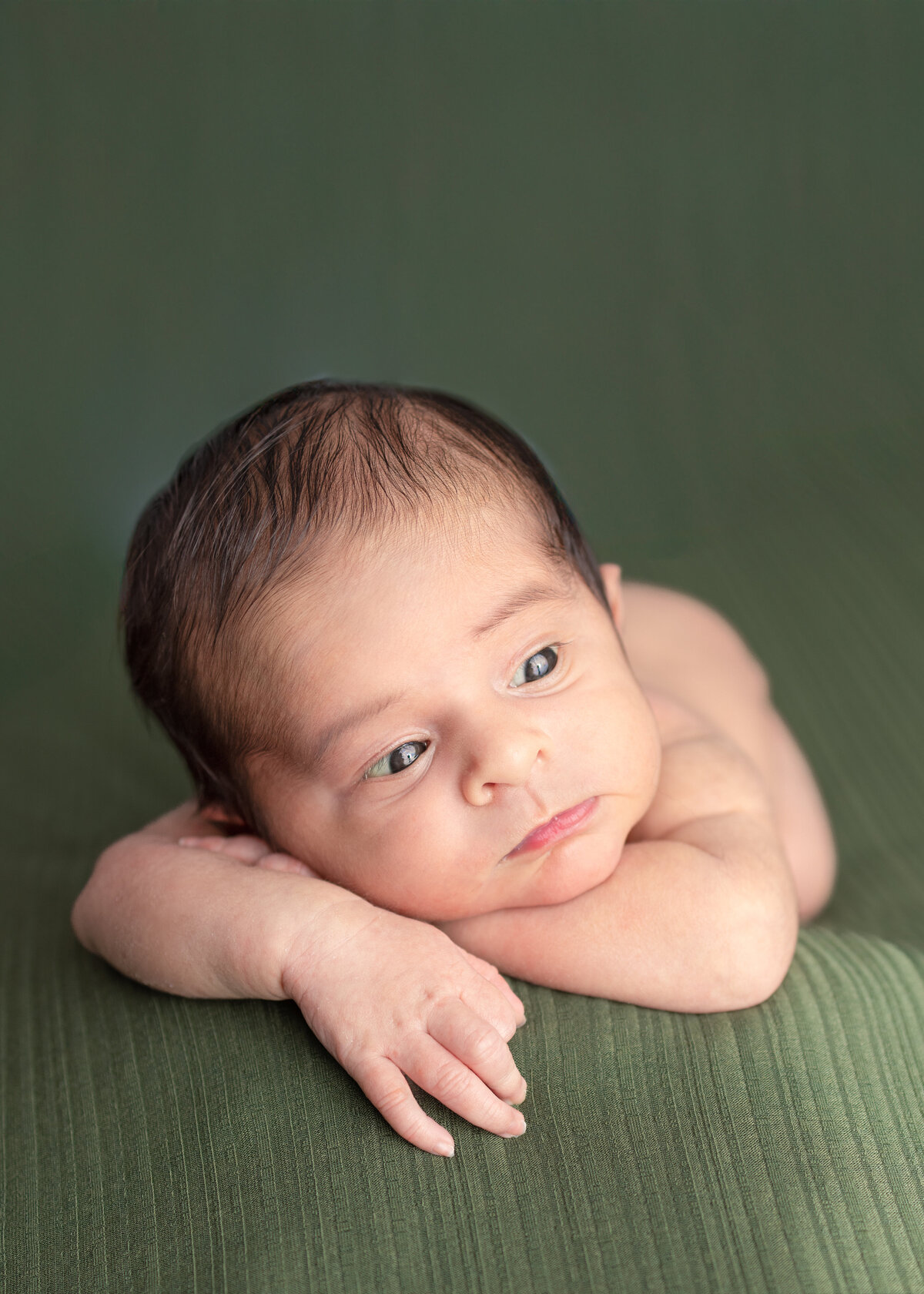 Baby boy laying on his belly with his head propped onto both his arms looking to the side during and in studio newborn session in Northern New Jersey.