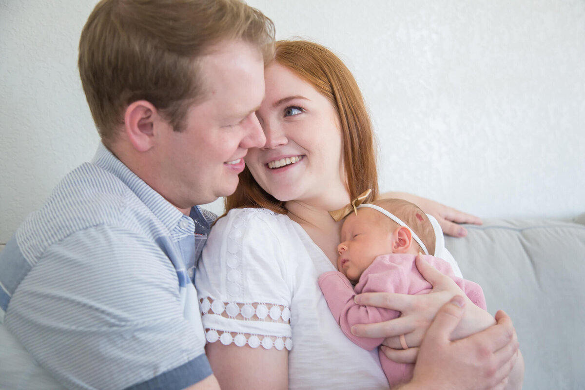 happy couple snuggling with newborn baby girl on gray couch at home