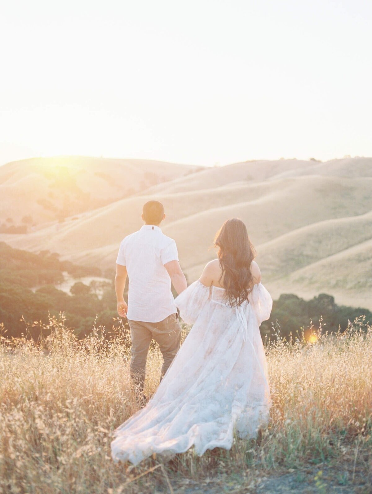 Maternity photoshoot in San Francisco with a pregnant woman and expecting dad standing in a field against hills.