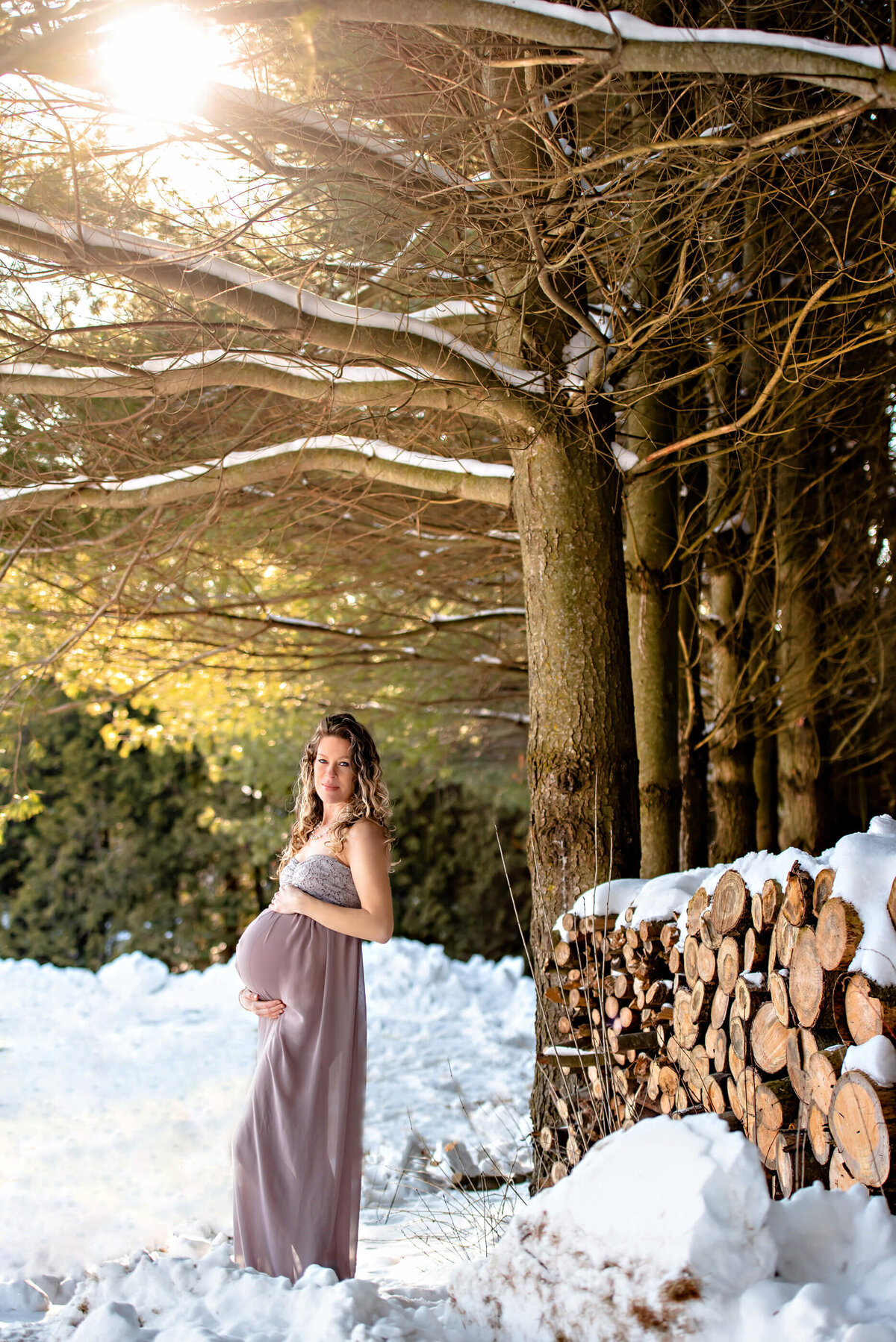 pregnant woman wearing a beige maternity dress outdoors in the snow for her outdoor maternity photography session
