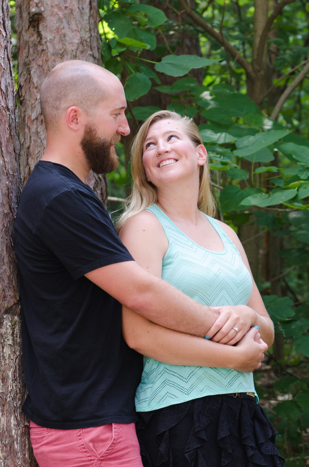 Bride-to-be looks up at fiancé leaning against a tree at Twin Lakes Park in Greensburg, PA