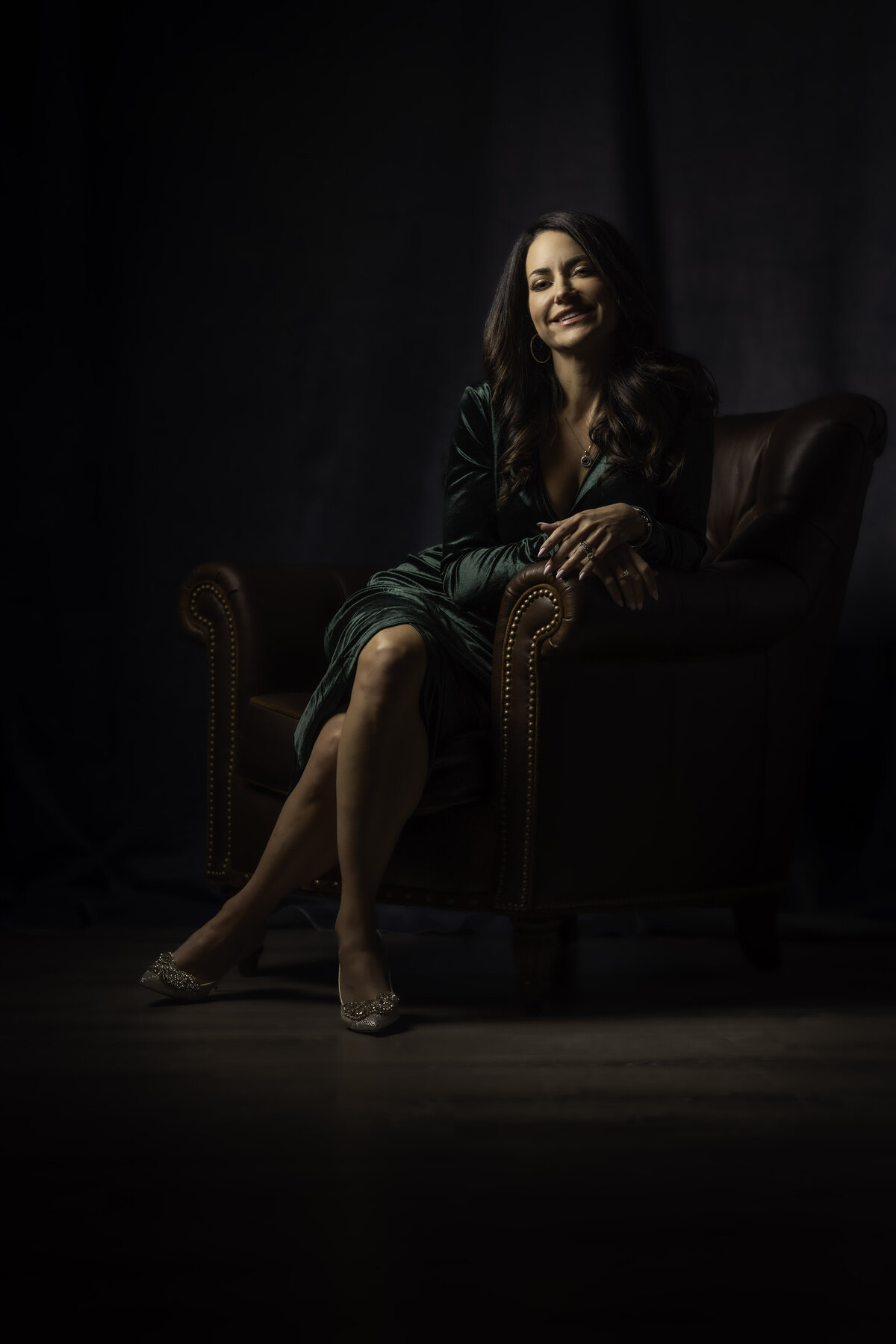 Professional business headshot in CT of a woman in a green dress against a deep brown background, photographed by Rob Faber Photography, specializing in headshots in CT and headshots in MA.