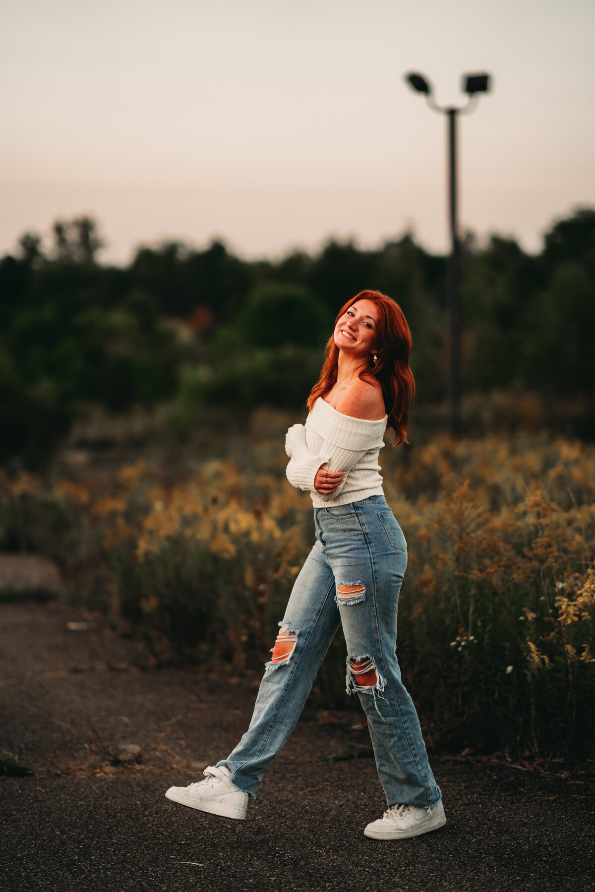High school senior twirls in a field at golden hour, with soft, moody lighting creating a warm & dreamy senior photo session.
