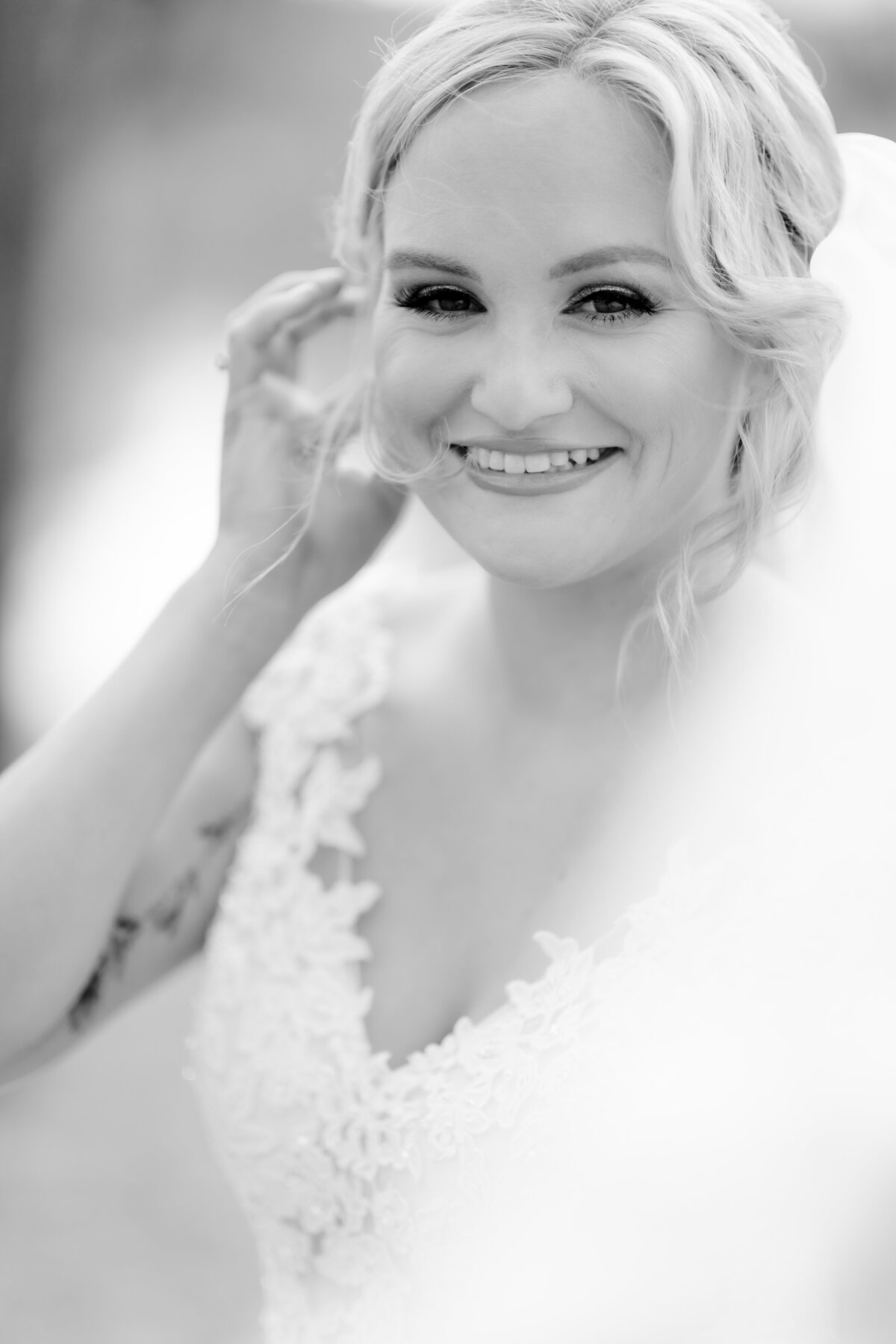 black and white wedding portraits captured by Little Rock wedding photographer with bride smiling and tucking her hair behind her ear while the wind blows her veil