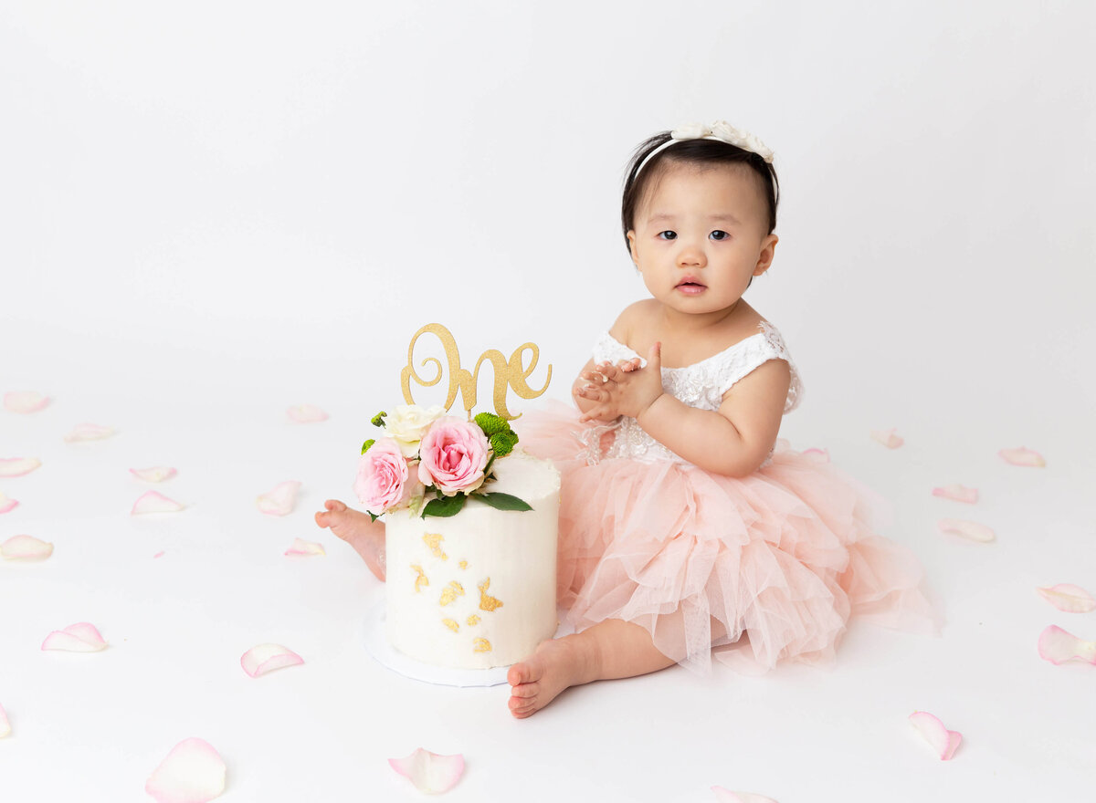 Cake smash photography in New York City featuring a baby girl enjoying their first birthday celebration with a pastel-colored theme. Capturing joyful moments for parents seeking memorable photoshoot NYC