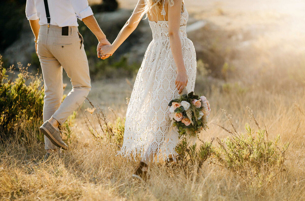 Bride & groom walking through a field at sunset.