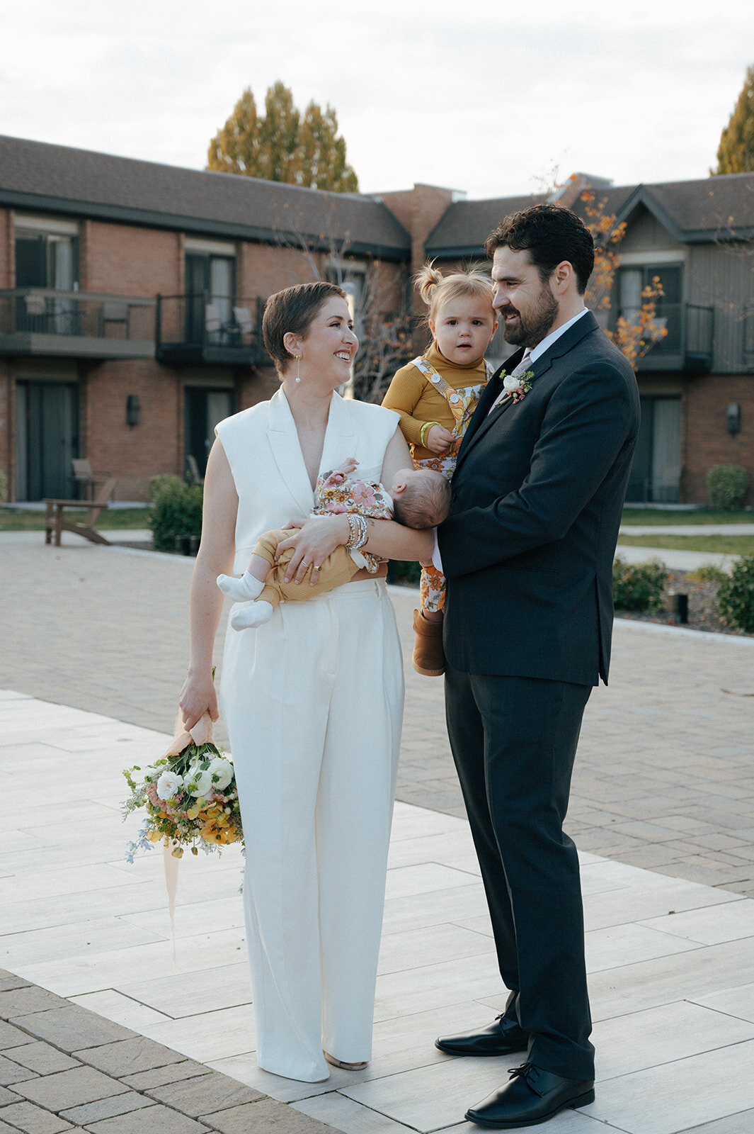 A bride and groom smile at each other of them are holding a young child.