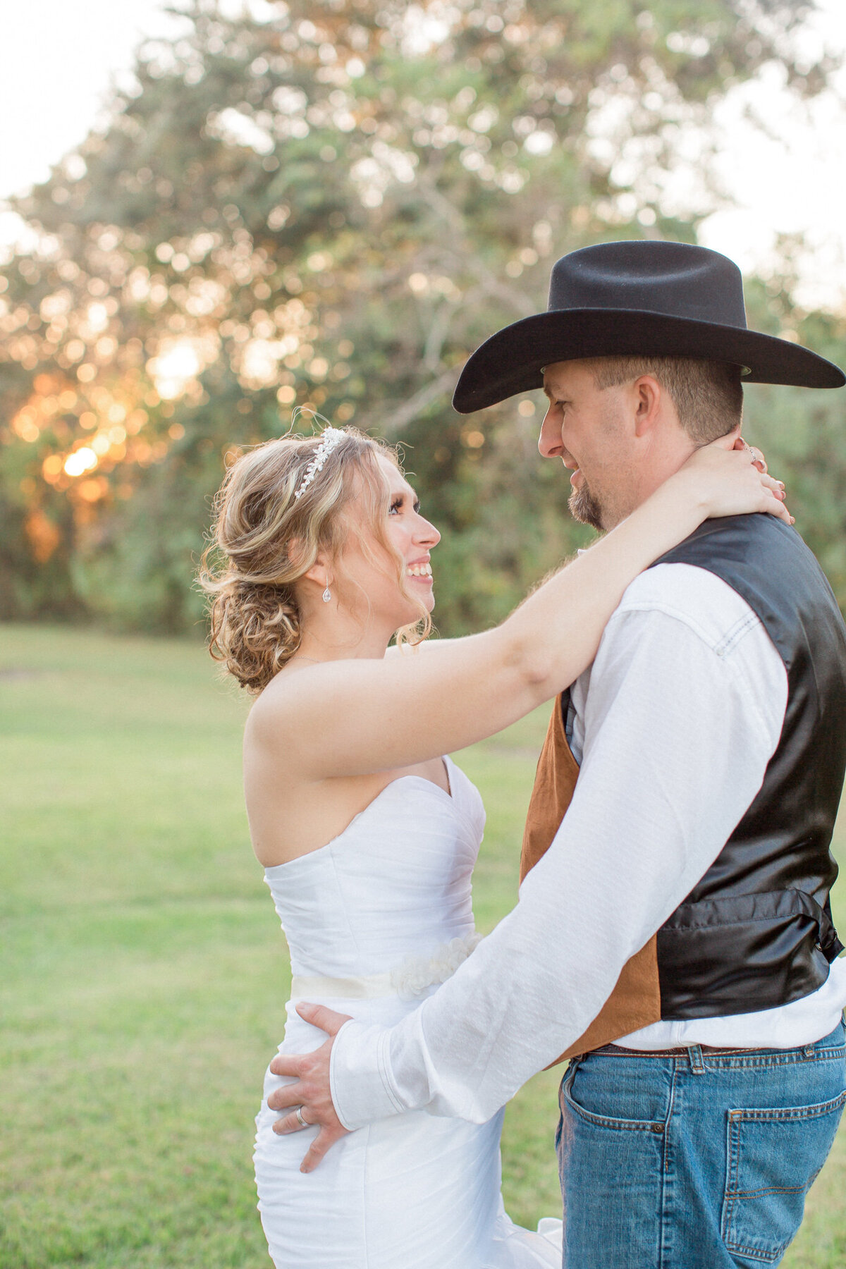 A bride wearing a tiara gazes at her Cowboy hat wearing husband
