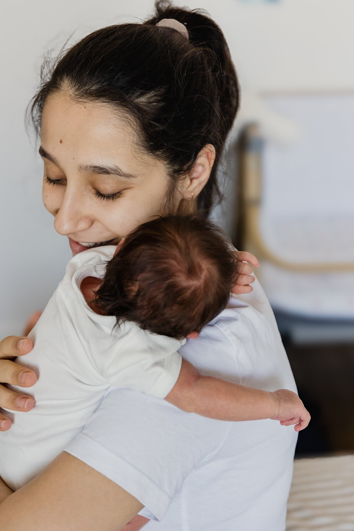 A woman gently cradling a newborn baby, both wearing white, with a tender expression on her face.