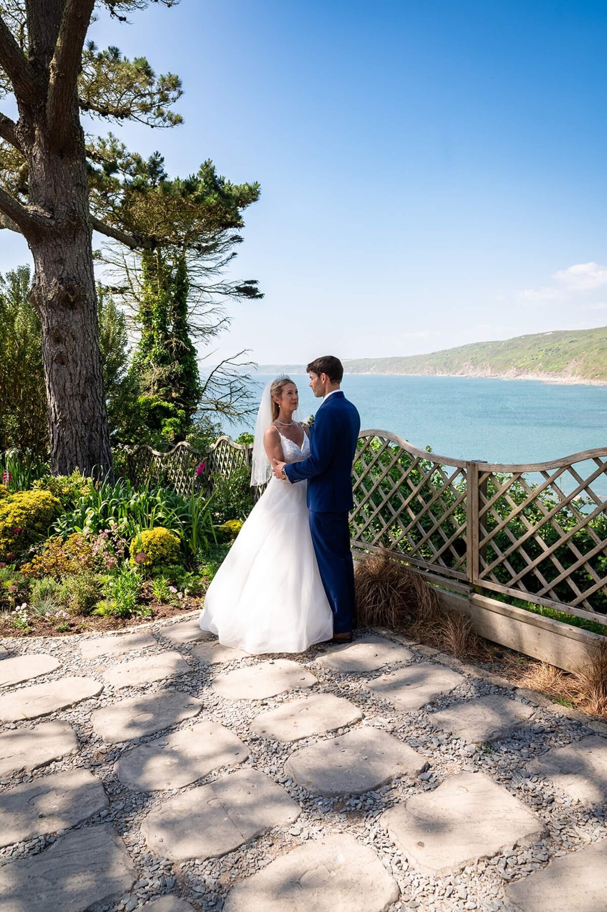 A bride and groom standing on a stone walkway overlooking the sea