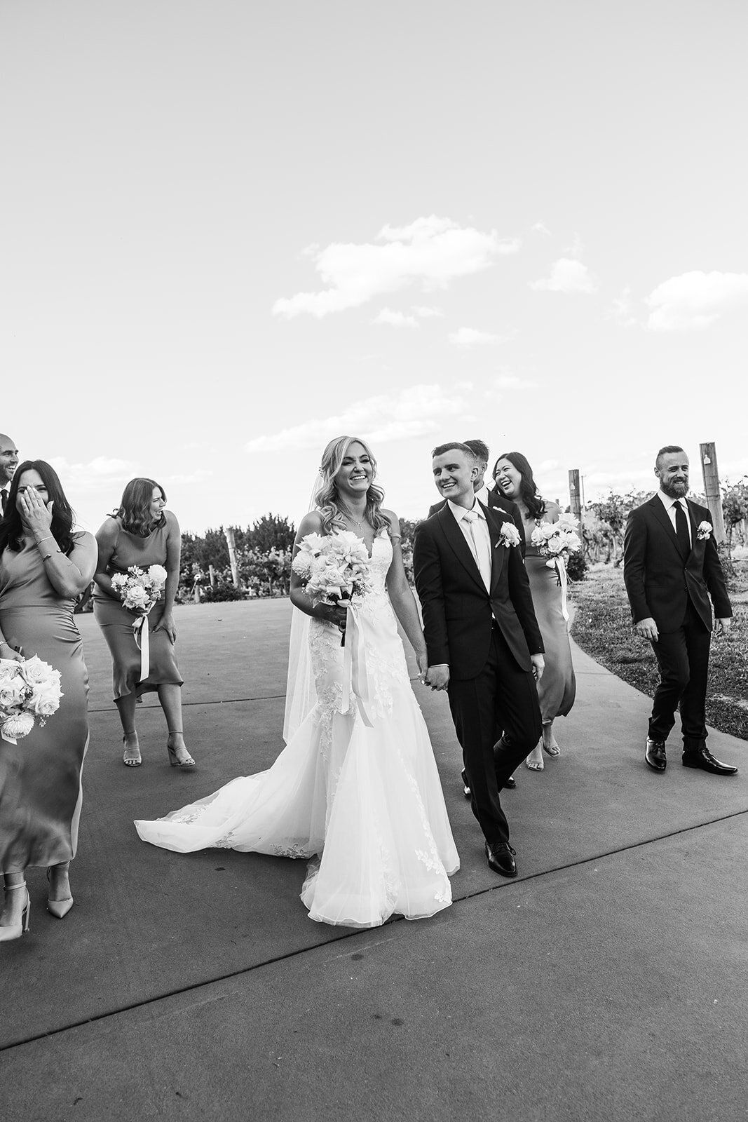 Black and white photos of bride and groom laughing while walking with their wedding party on the driveway of Brindabella Hills Winery