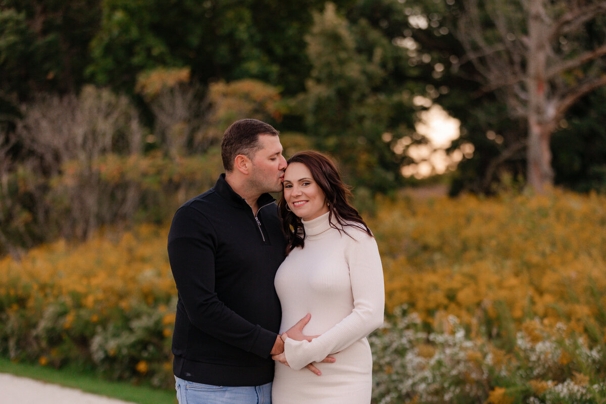 Dad kisses moms forehead while they hold her belly during a maternity session.