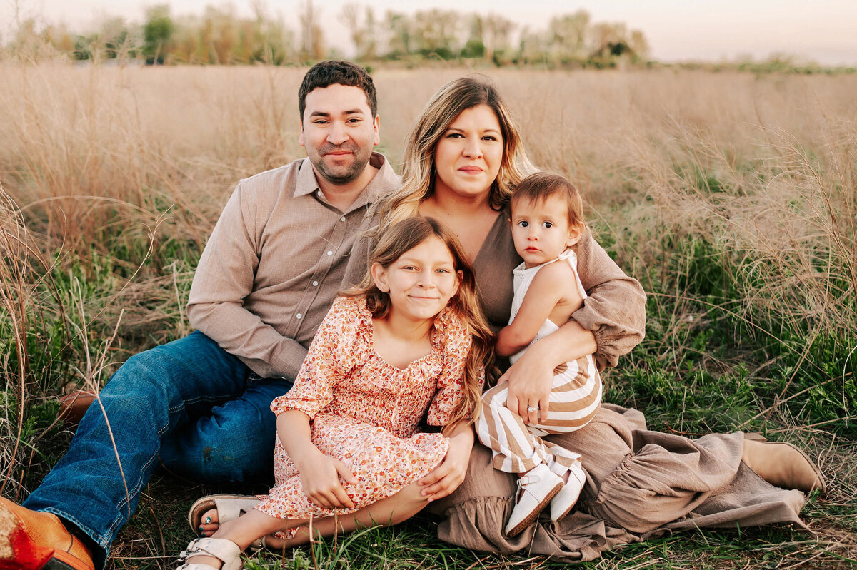 family sitting in a field smiling at sunset enjoying Branson MO family photography