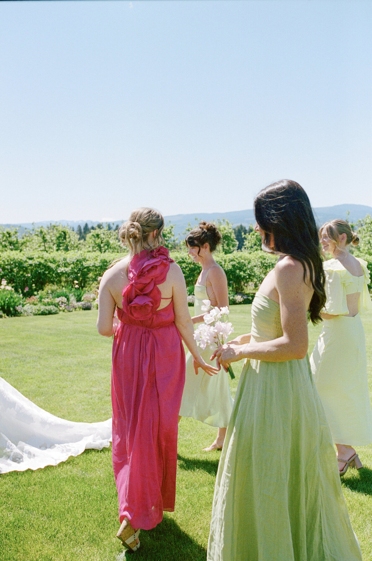 Bridesmaids in colorful pink and green dresses walking at The Orchard in Hood River.