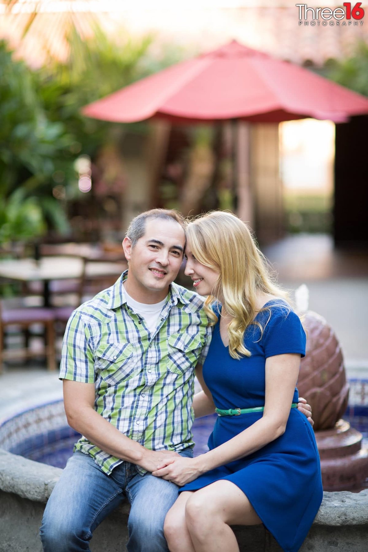 Engaged couple cuddle up while sitting on the edge of a water fountain at the Villa Del Sol