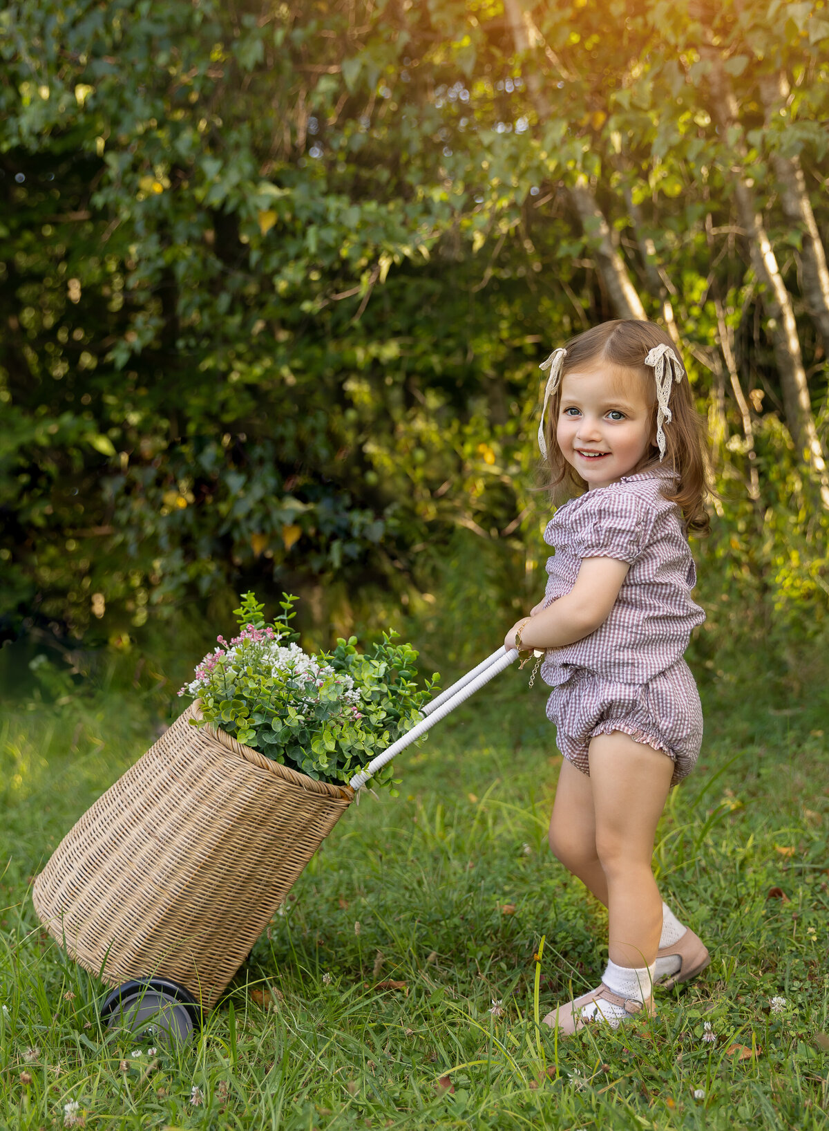 Little girl in a lavender romper is holding a basket of flowers for her brooklyn ny photoshoot. Captured by brooklyn family photographer Chaya Bornstein