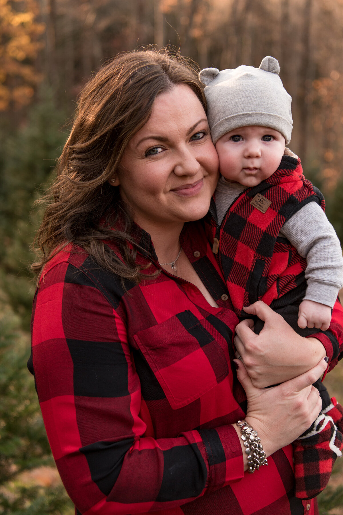 Mother in red buffalo plaid shirt holding infant son and smiling