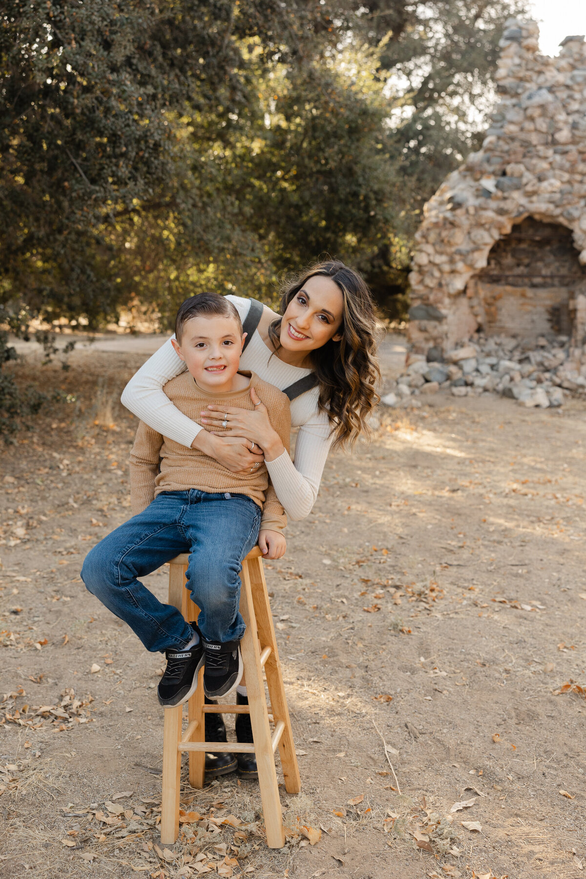 Mother holding son on her lap while sitting on wooden chair outdoors. Photographed by Yucaipa family photographer Kaitlyn Dawn Photography.