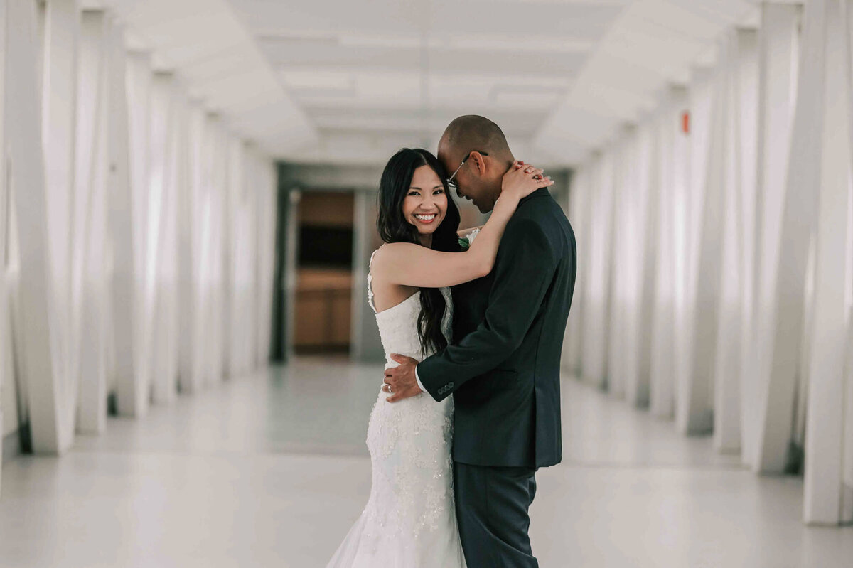 Bride and groom are facing each other. Bride is looking at camera, and groom is looking at bride.