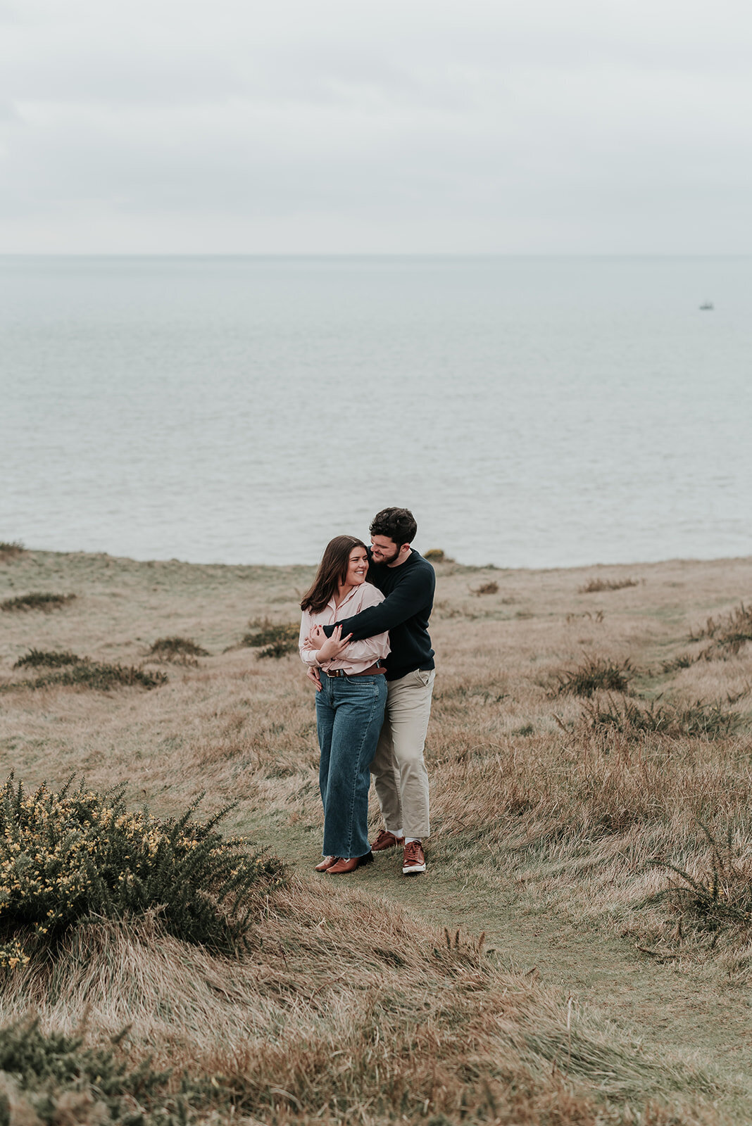 Couple cuddle standing together on the South Downs and Beachy Head Eastbourne
