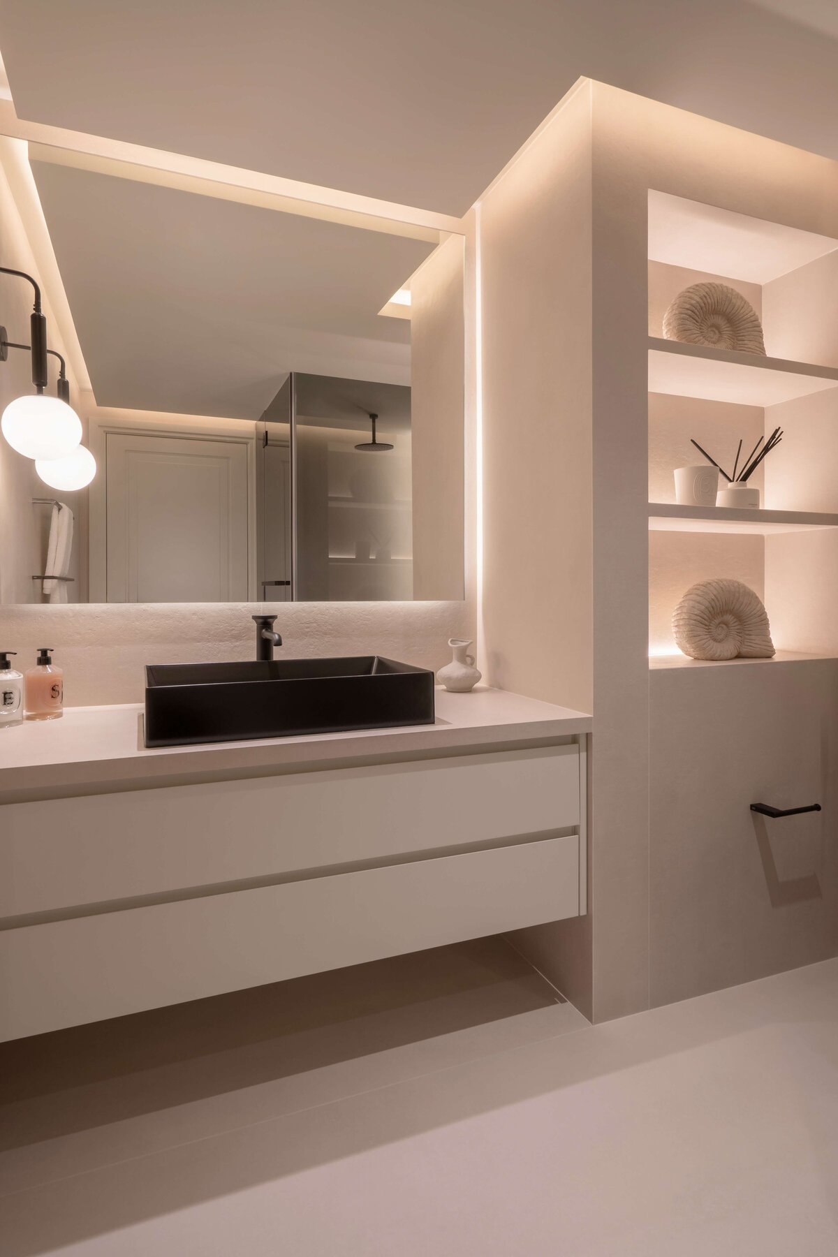 Spacious bathroom with a focus on light, neutral tones. Large built-in shelving emits a soft light. A black sink adds contemporary flair to the space.