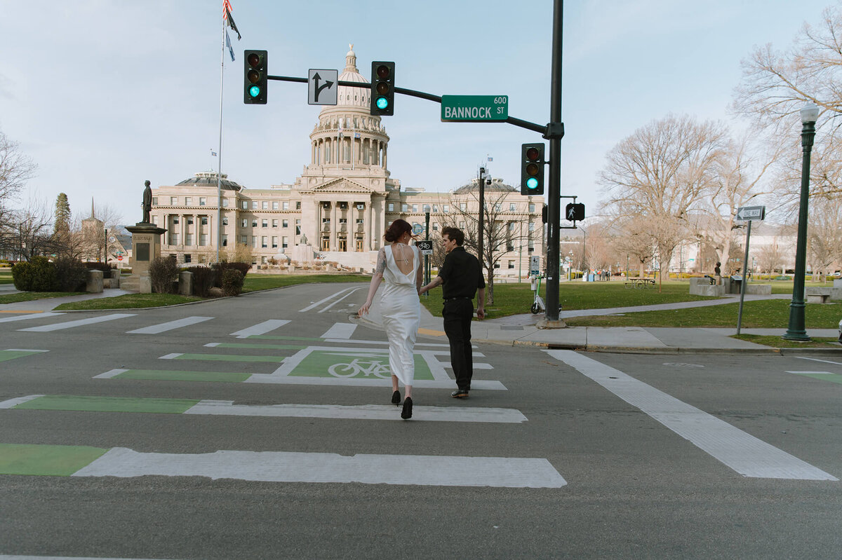 A man and woman run across a crosswalk in downtown Boise in front of the capitol building.